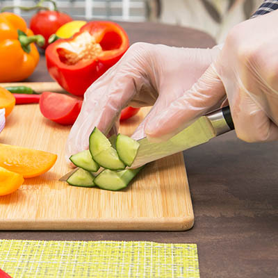 Hand wearing a clear glove chopping up cucumber and tomatoes.